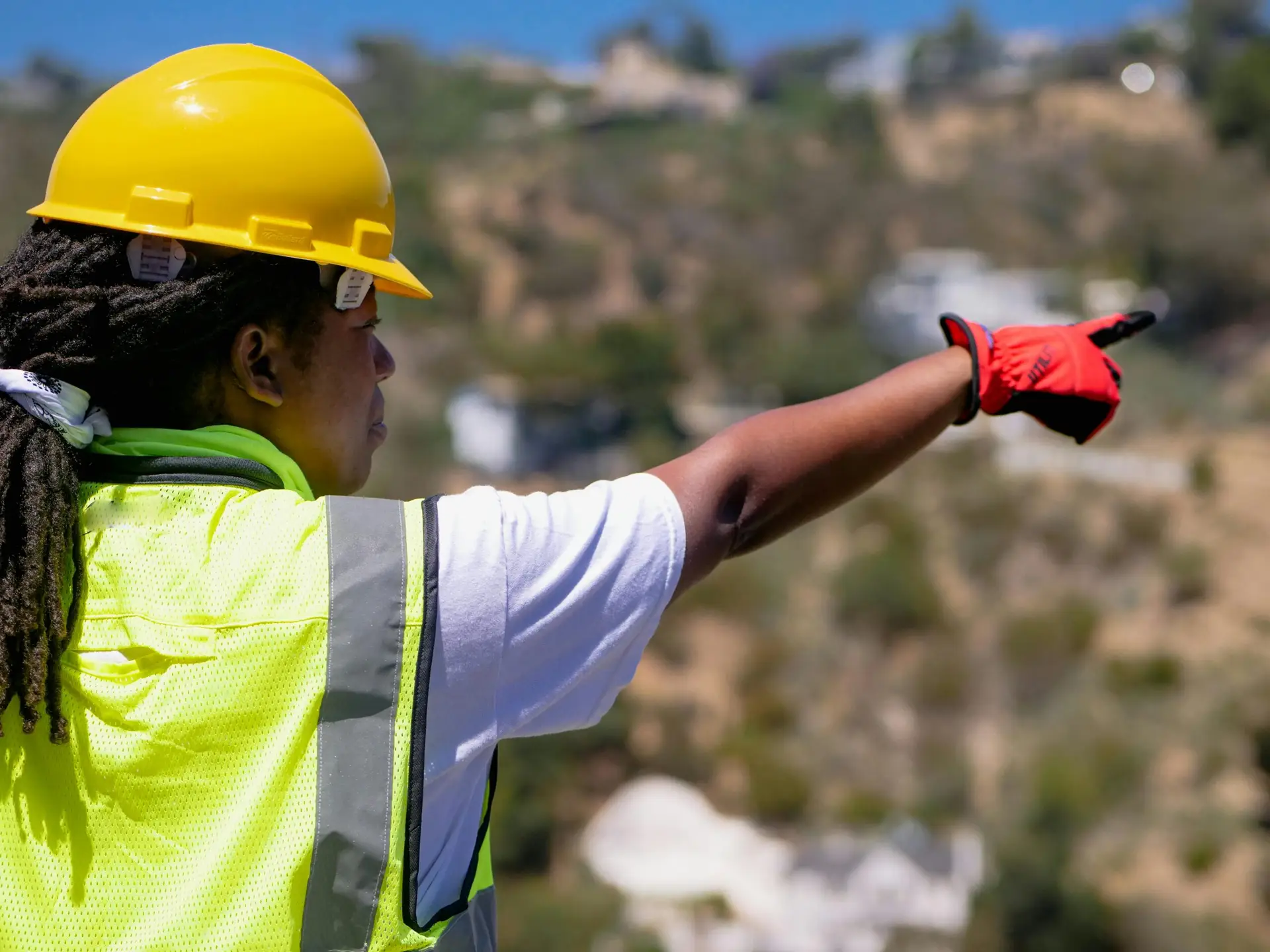 Black female engineer in safety gear pointing at a construction site.